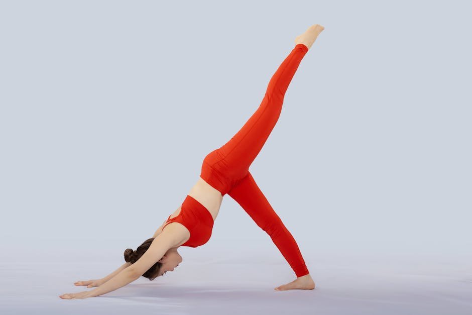 A woman doing a yoga pose in a studio, wearing vibrant red sportswear on a neutral background.